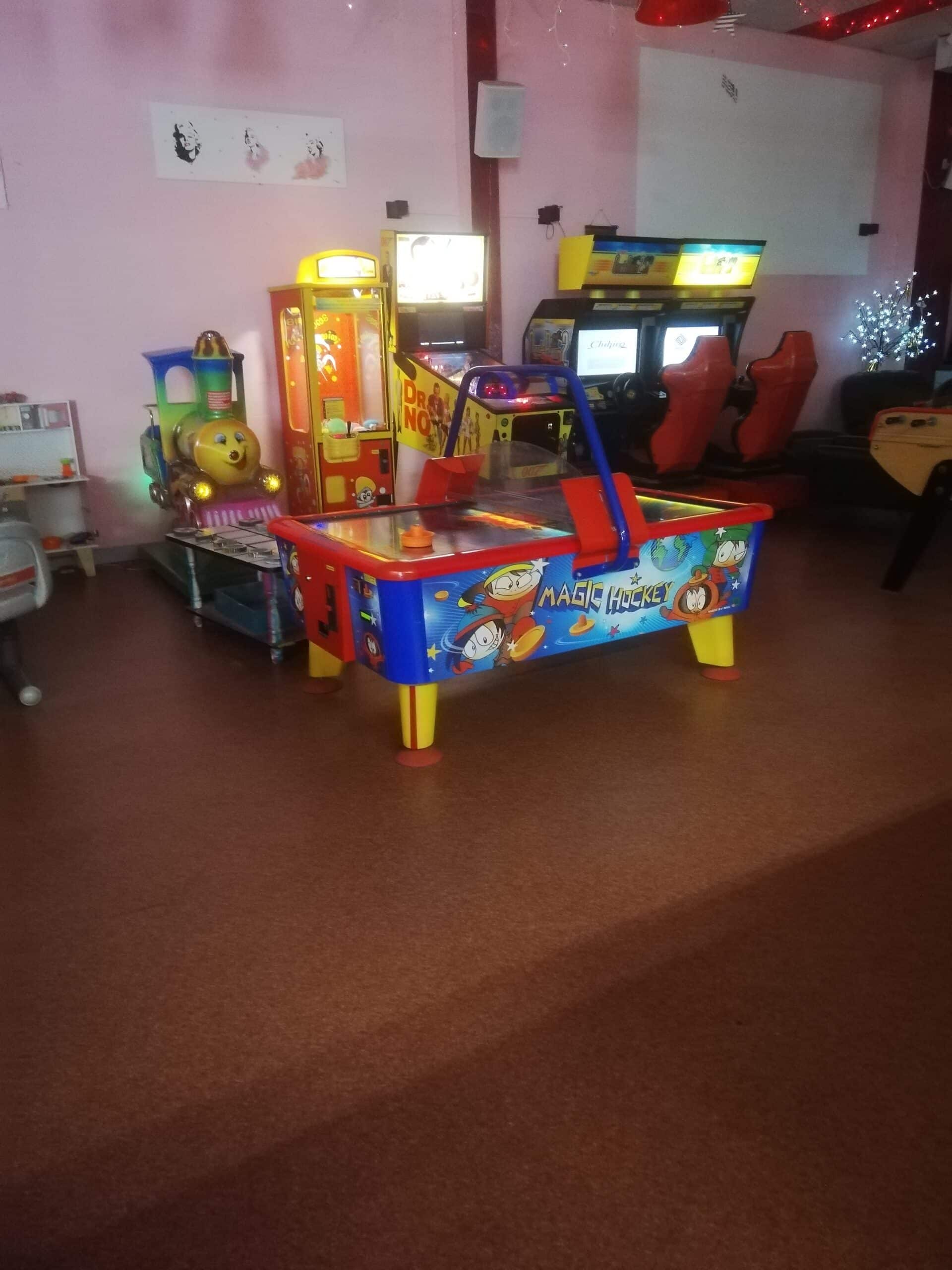 Salle d'arcade lumineuse avec table Air Hockey Magic, jeux vidéo de course 007, machine à griffes et manège enfant train souriant. Décorations murales Marilyn Monroe.